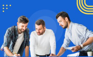Three men collaborate at a desk, writing and reviewing notes together against a blue background with yellow accents.