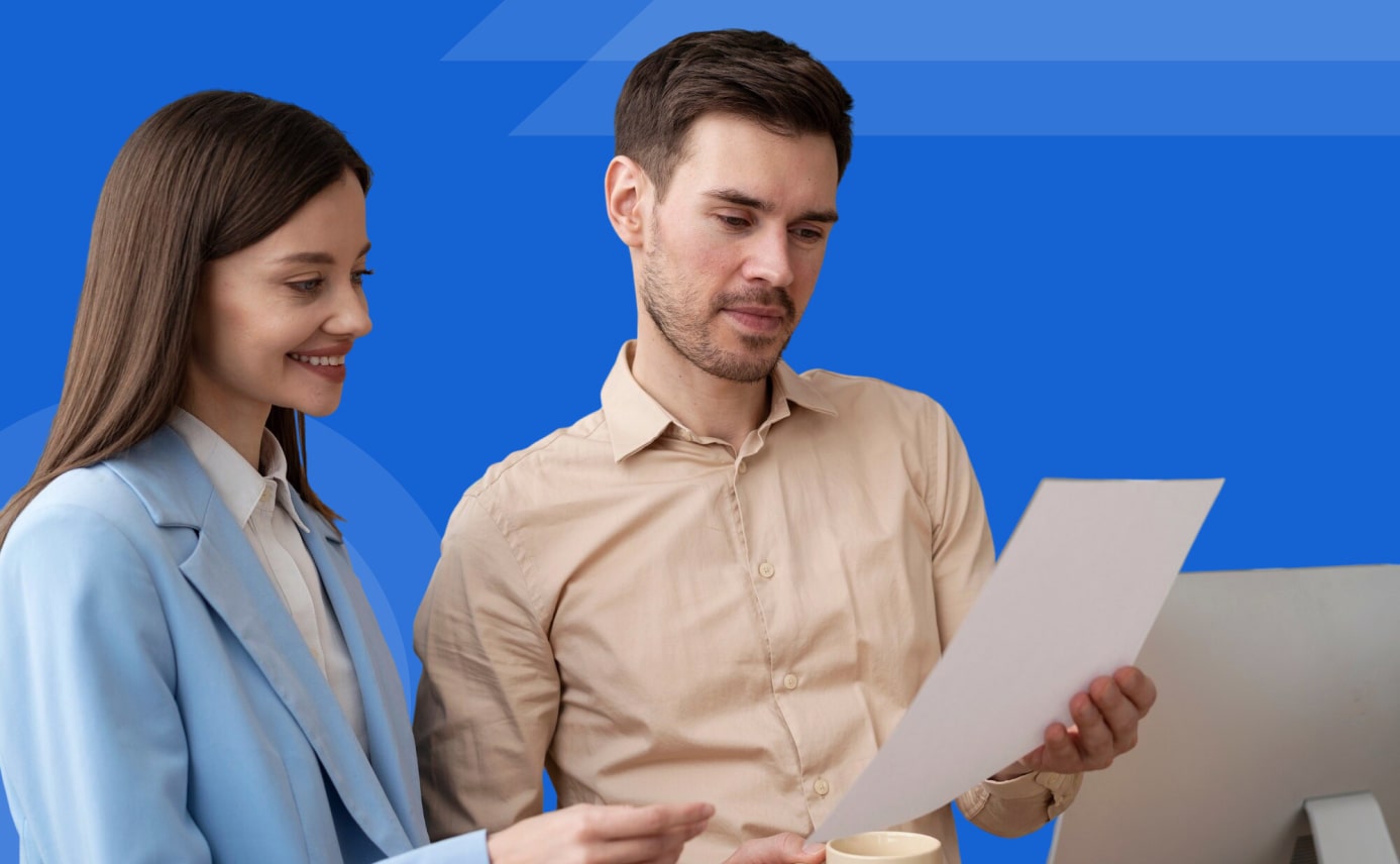 Two professionals reviewing a document together while standing near a desk with a blue background