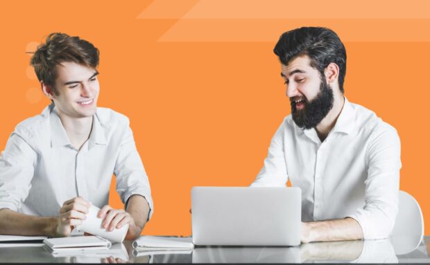 Two colleagues collaborating at a desk with laptop and papers on an orange background