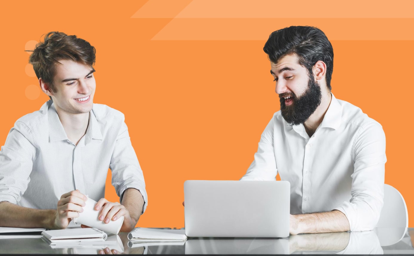 Two colleagues collaborating at a desk with laptop and papers on an orange background