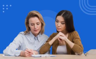 Two women sitting at a table reviewing notes together against a blue background